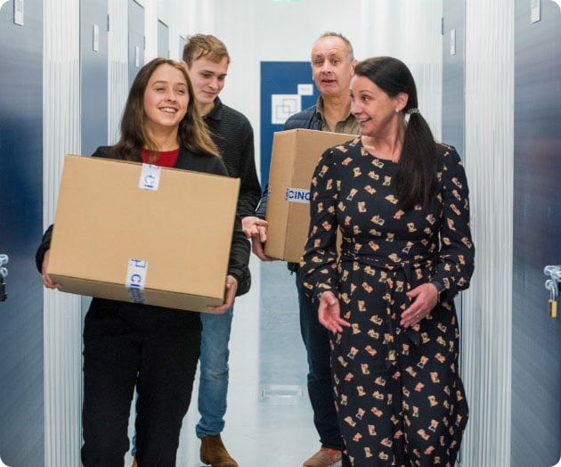Two people carrying boxes while talking with their friends through a hallway