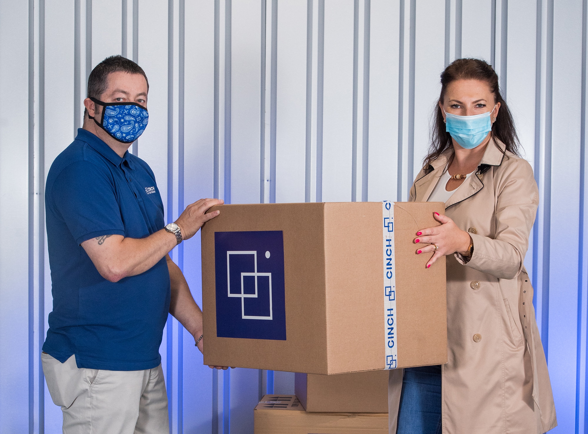 A man and a woman wearing a face mask holding a cardboard box inside a storage unit