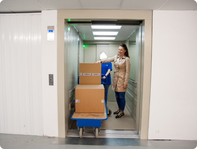 A woman touching a cardboard box on a trolly in an elevator