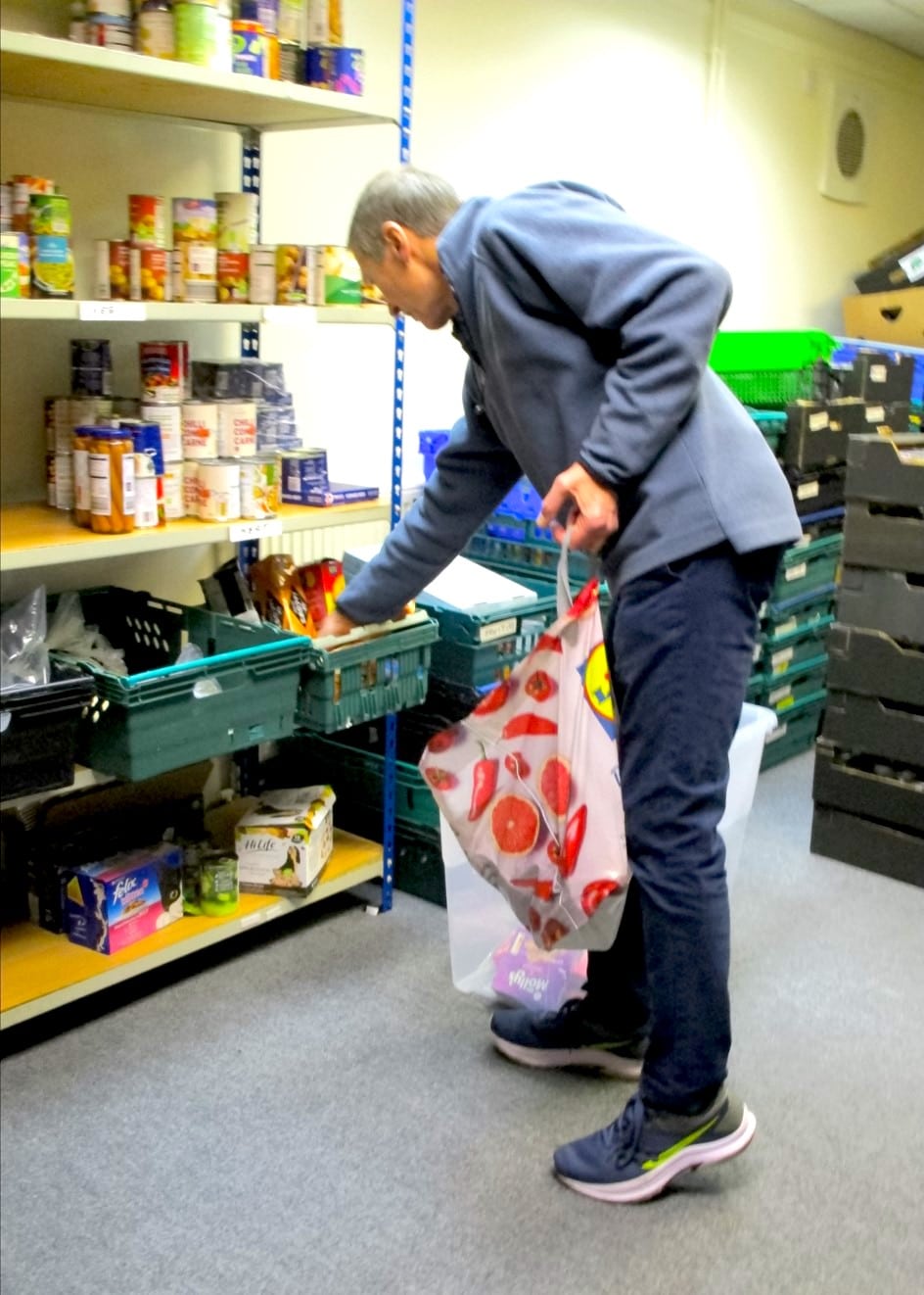 A man leaning to reach into a basket of food on a shelf