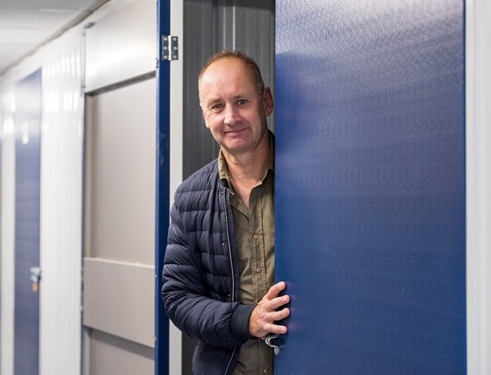 Man half behind blue door in storage facility facing camera and smiling