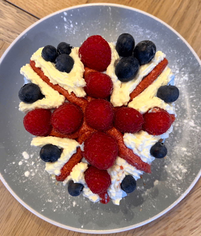 Aerial view of a homemade cake decorated with a Union Jack out of fruit and cream, on a grey plate.