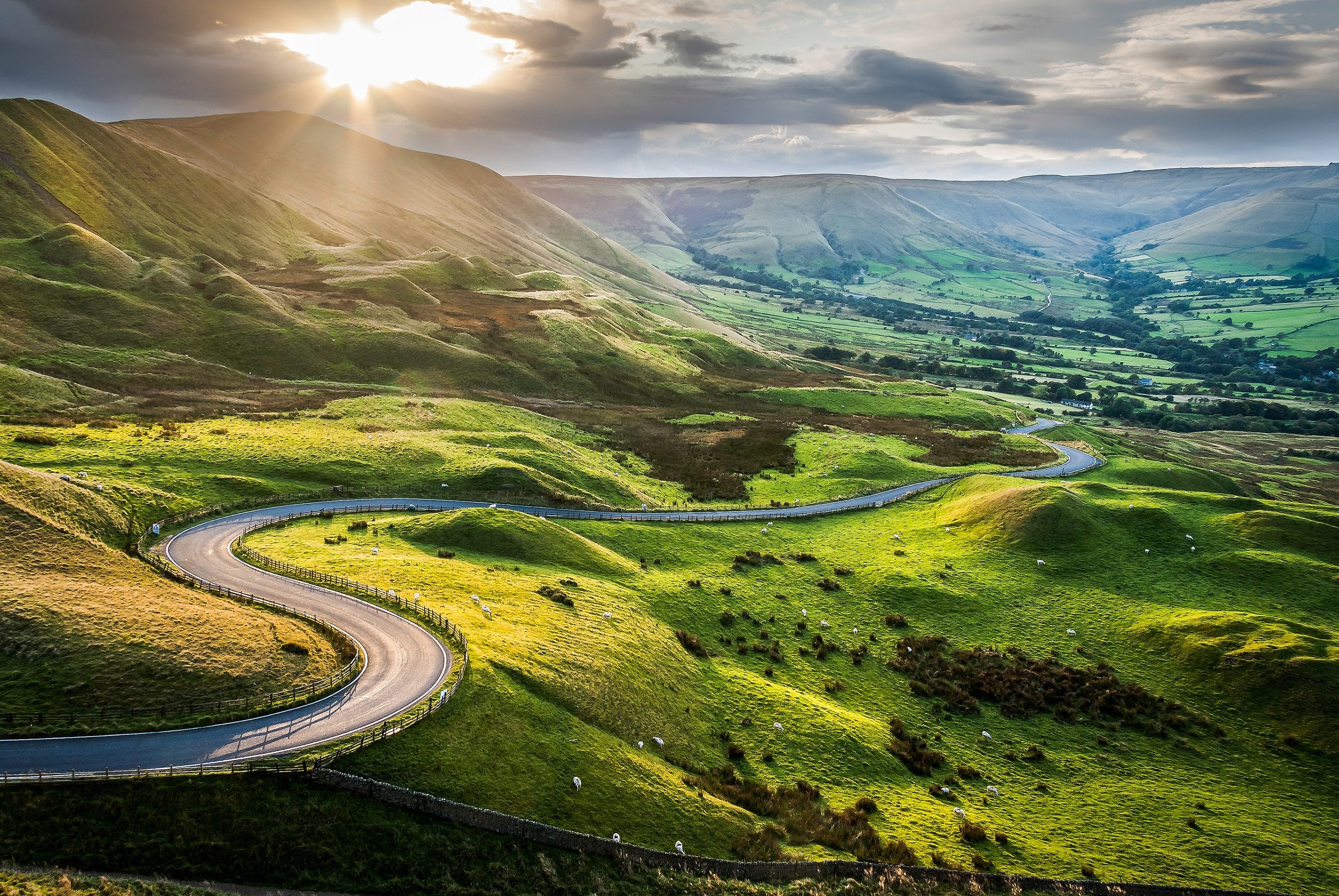 A view of a sunset along a winding road among green hills