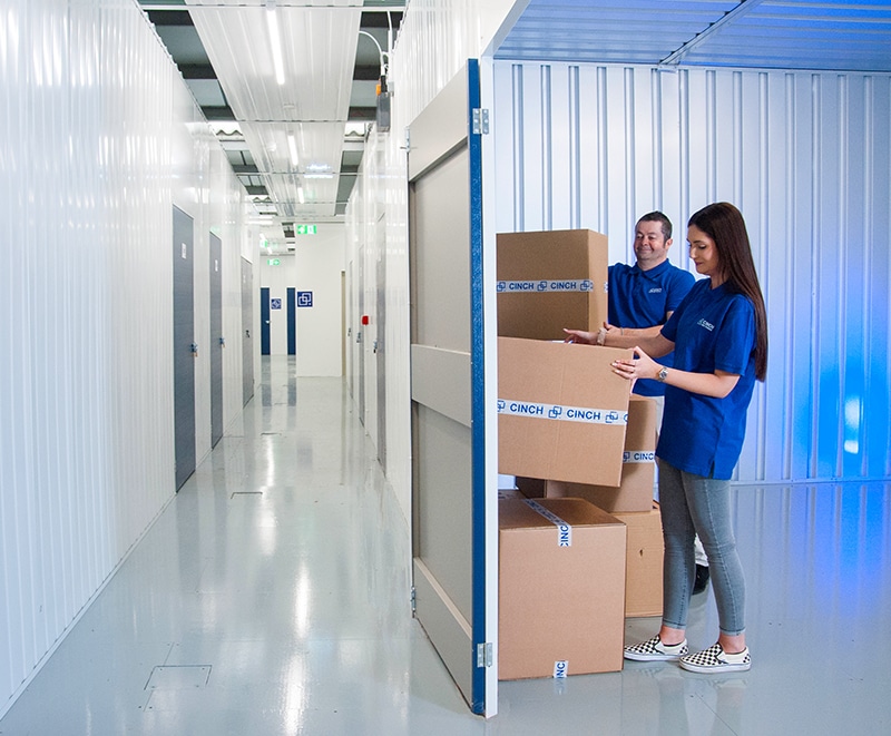 Self storage Newbury - photo shows inside of storage unit with two people stacking boxes and the corridor of storage units to the left
