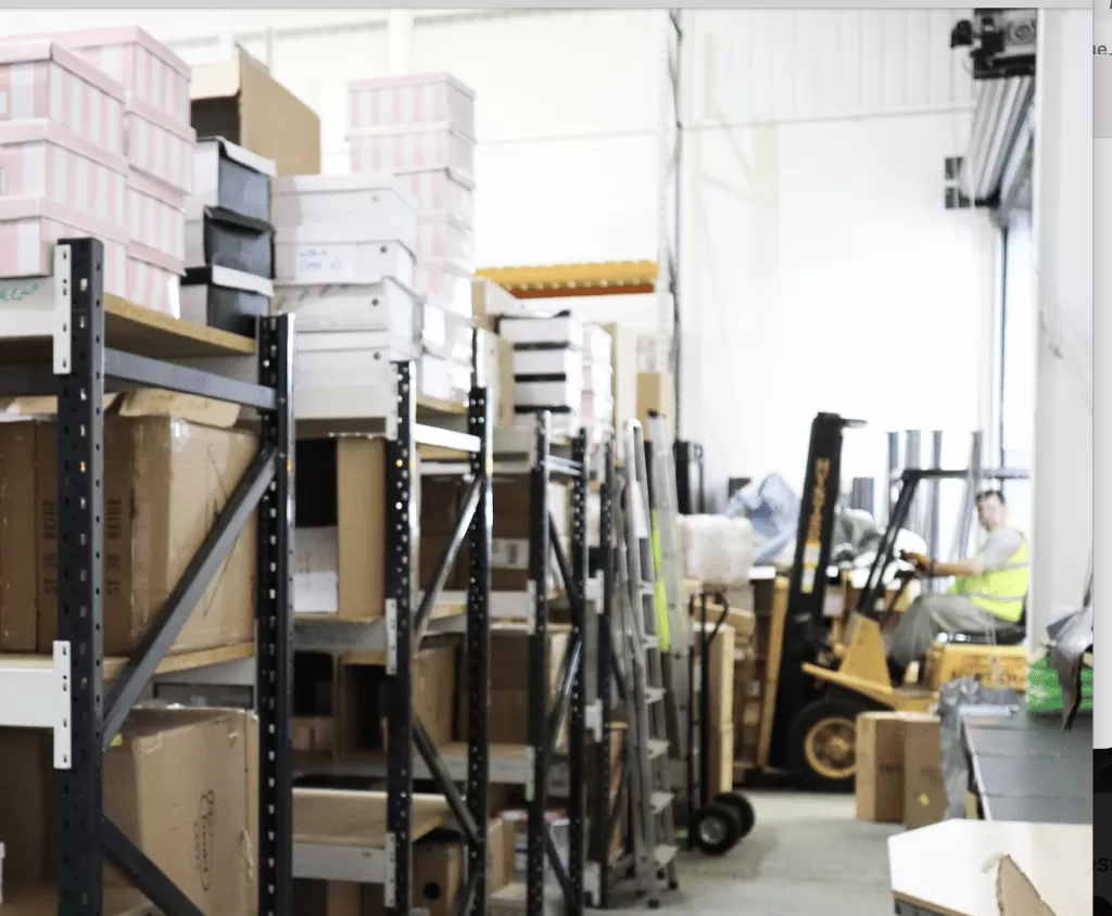 Enfield storage - interior of storage space showing racking with shoe boxes stacked on top and a forklift with a driver inside