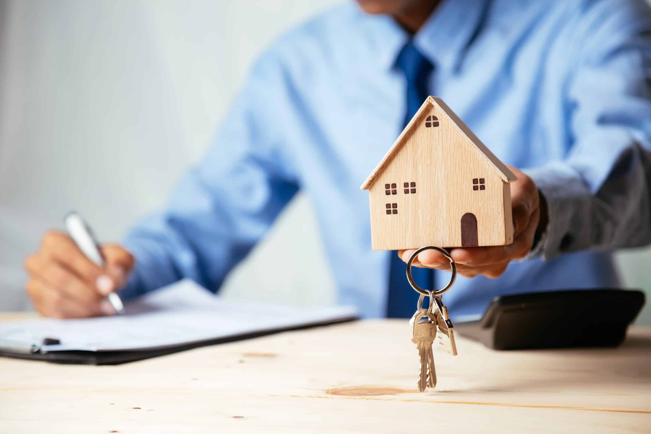 Storage Letchworth UK - image shows a man holding a wooden house model and keys to a new home he is wearing a blue shirt and tie, sitting at a desk with one hand holding a pen and signing a paper