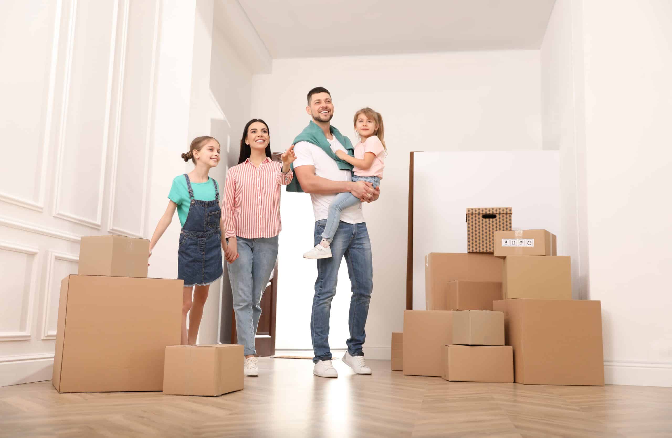 Photo shows a family of 4 standing in their new home surrounded by moving boxes