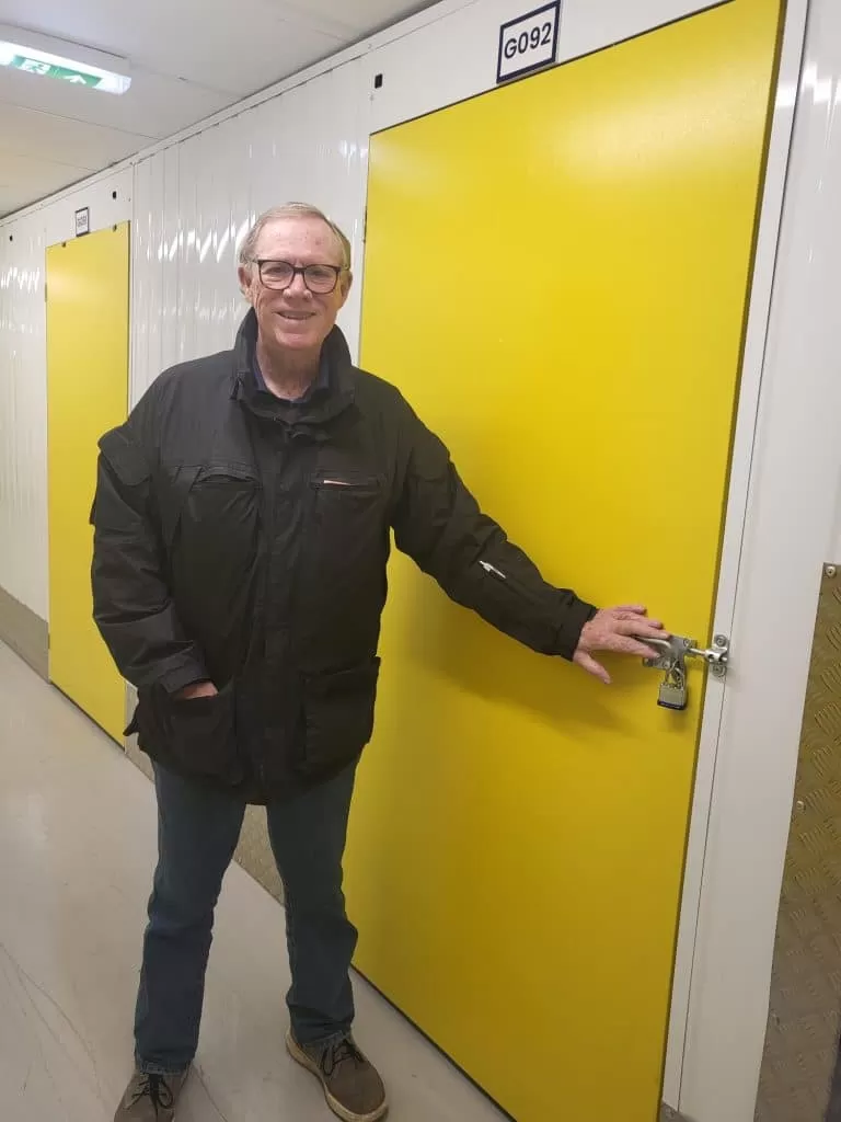 Cinch Self Storage Case Study - Photo shows a man, Cy Wells in front of his storage unit with a yellow door