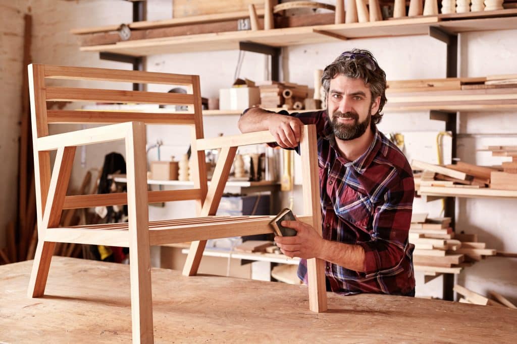 Newbury storage - image shows a man in his storage space with shelving holding tools and him standing at a central workbench sanding down a wooden chair