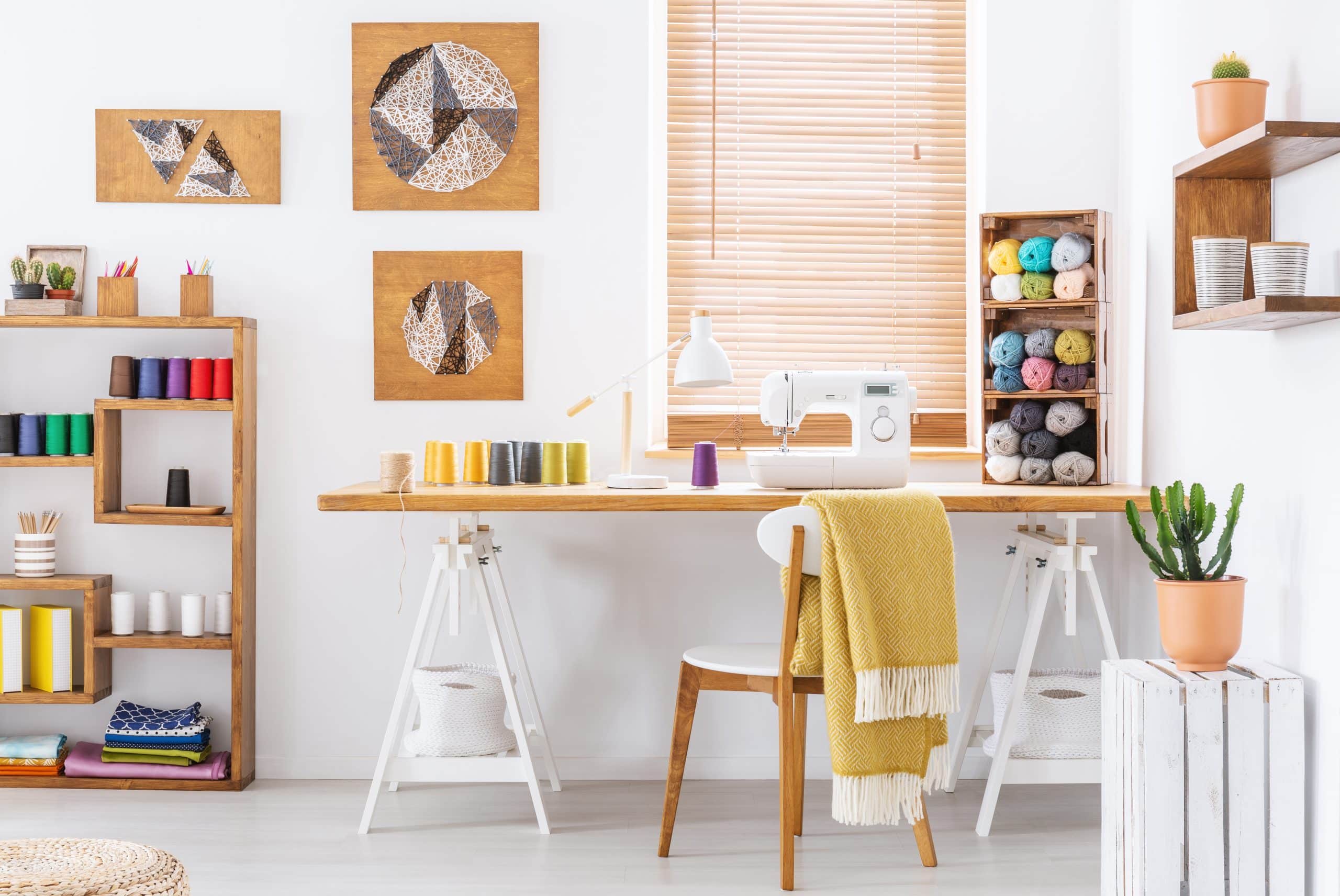 Storage units Bicester - image shows a hobby room with a desk against a wall with a window, a yellow blanket draped over the chair and shelves with wool, a sewing machine and threads on the desk and paintings on the wall