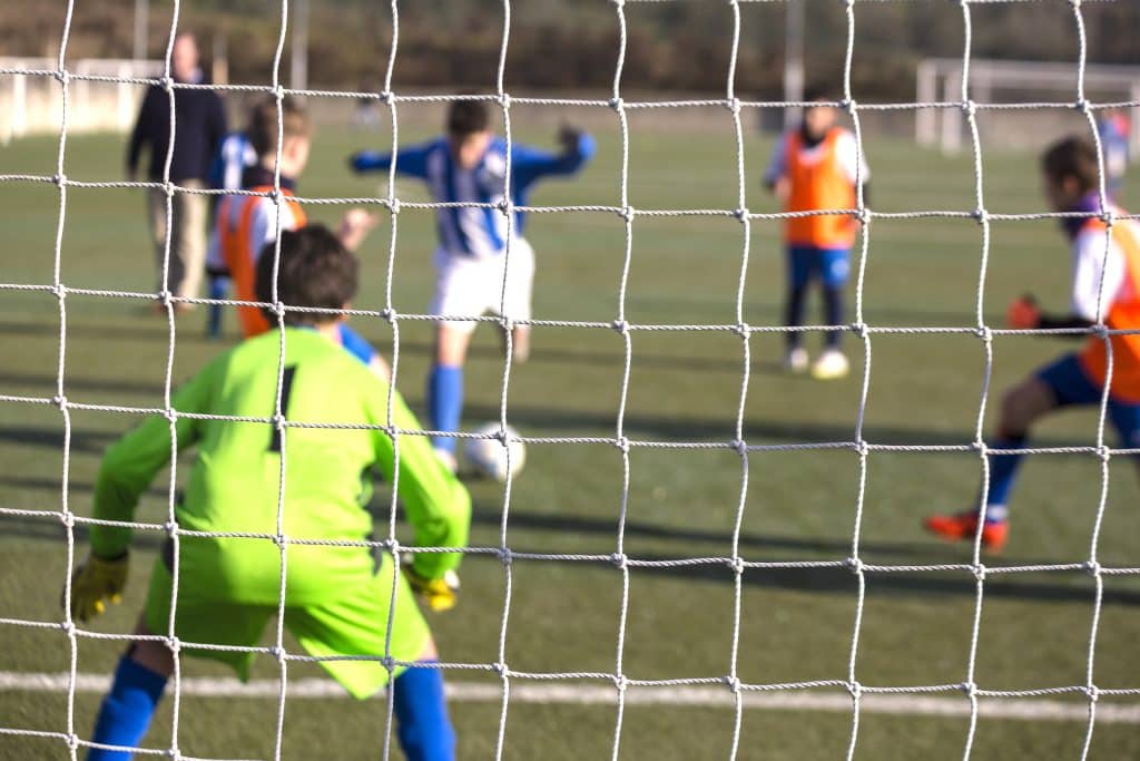 Storage units to rent Brighton - image shows looking through a football goal with a goalie in goal with a green kit and then another player taking a kick on the ball in a blue and white striped kit 