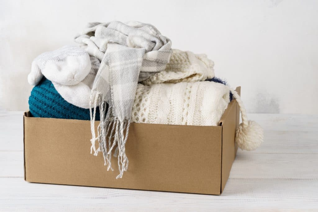 Seasonal Storage: Our storage Brighton can help you find space. Image shows a cardboard box filled with winter clothing - a grey scarf, white jumper, blue wool and white woolen socks