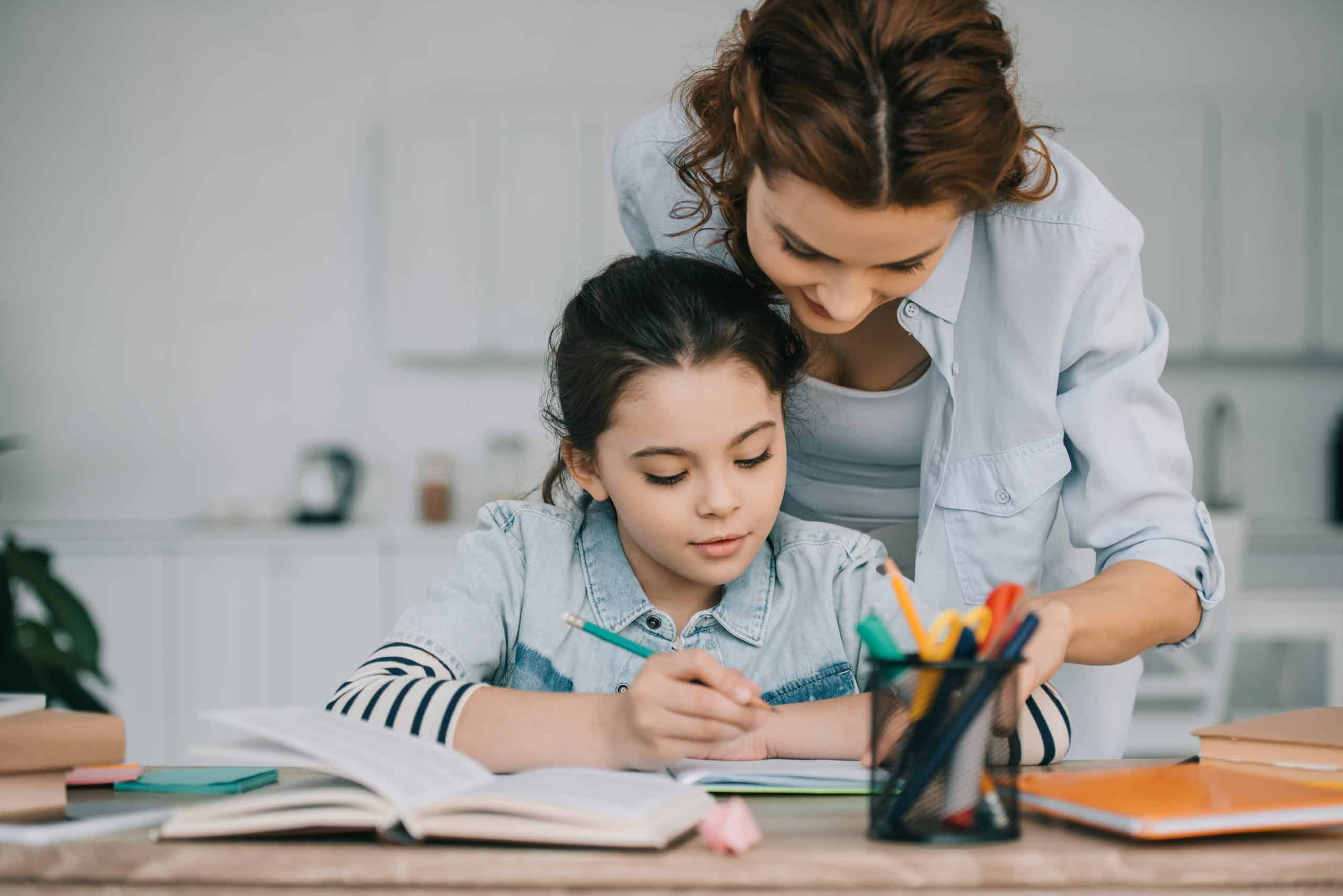 Decided to homeschool? Our storage near Newbury will help you make room. Image shows a mother and a daughter sat at the table with a pen pot and looking at books together.