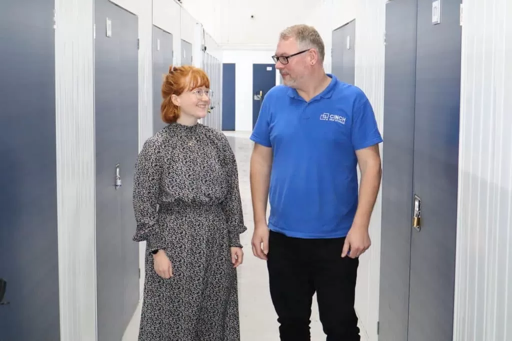 Going home for the summer? Our Brighton storage units will help. Image shows a female student and a member of the Cinch Self Storage team standing in the corridor with storage unit doors on either side of them.