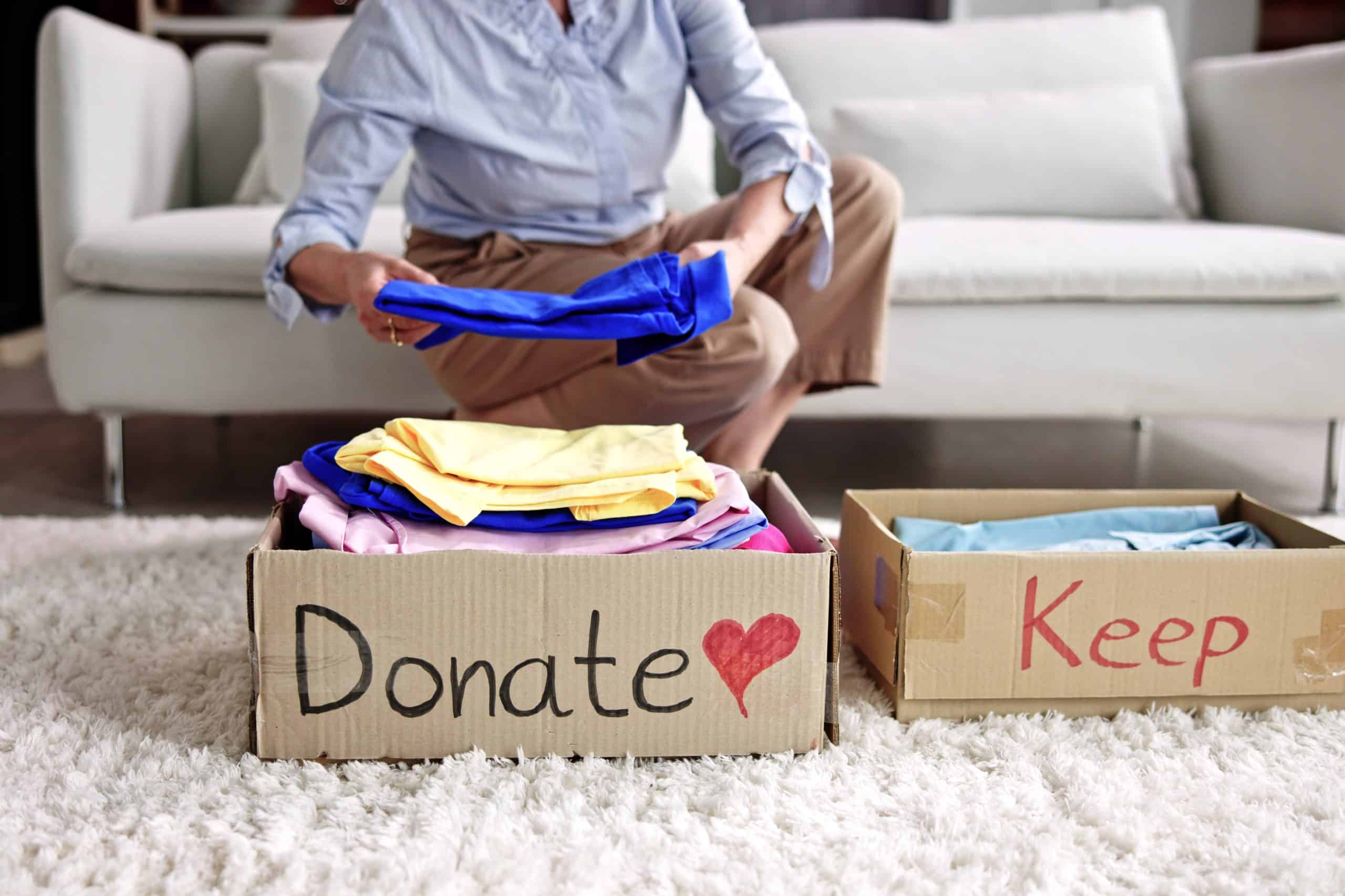 Decluttering your home - image shows a person putting a blue t-shirt into a cardboard box labelled 'Donate' and another cardboard box alongside is labelled 'Keep'