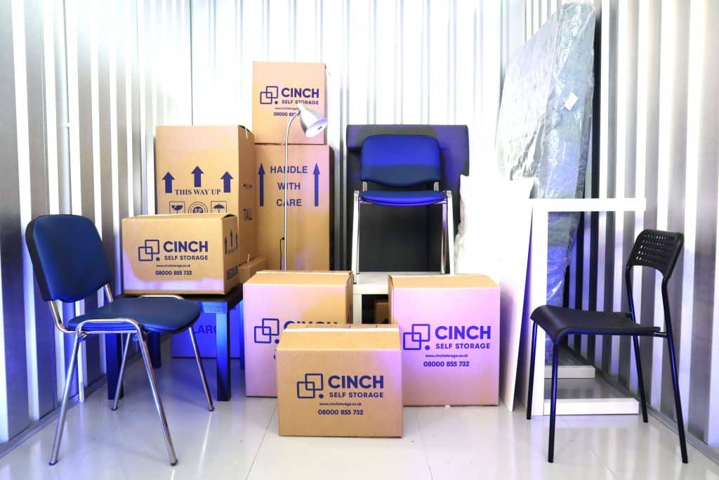 Furniture Storage Cinch Self Storage - image shows the inside of a storage unit with Cinch Self Storage boxes stacked within it along with chairs, a sofa and mattress 
