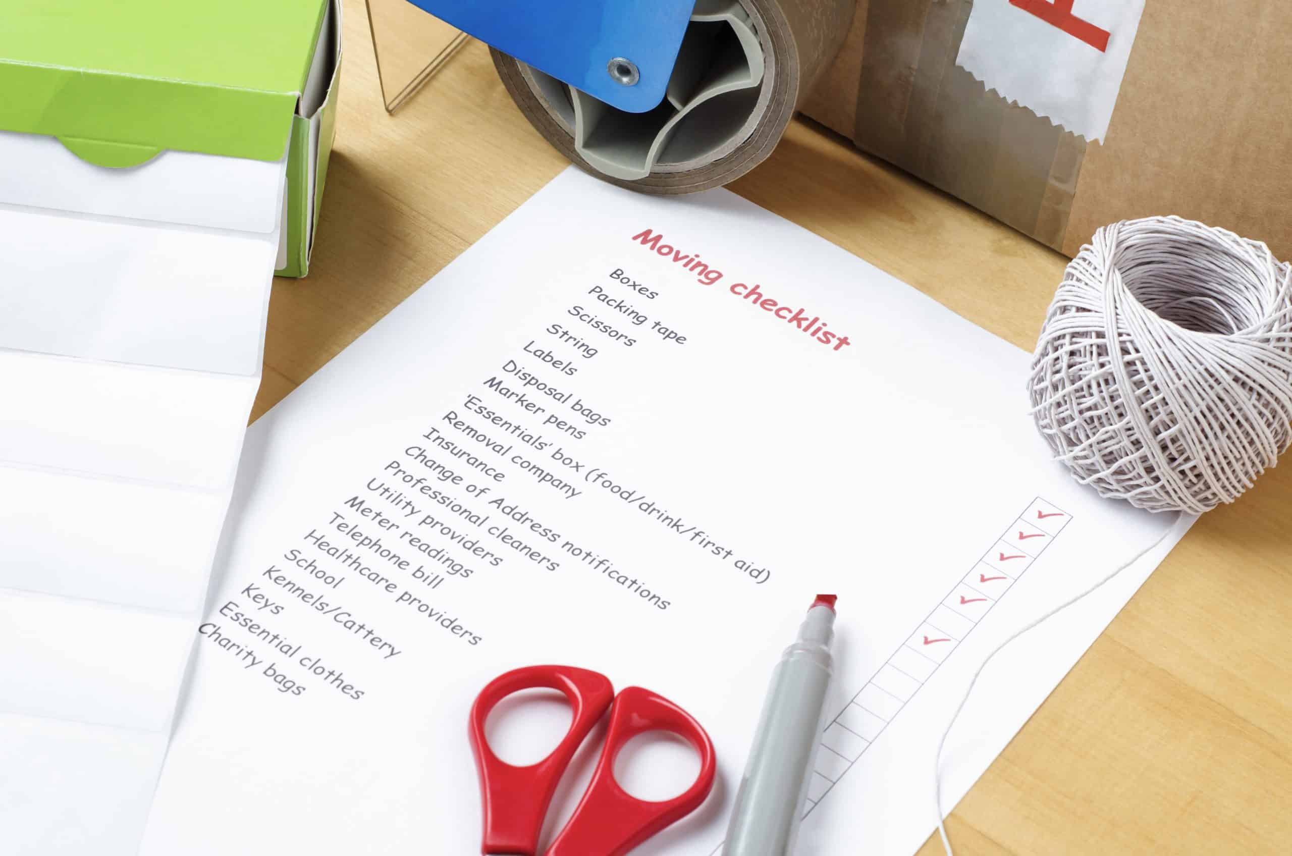 Moving House Storage - image shows a moving checklist printed on a piece of paper laying flat on a cardboard box with scissors, pen and tape gun surrounding it