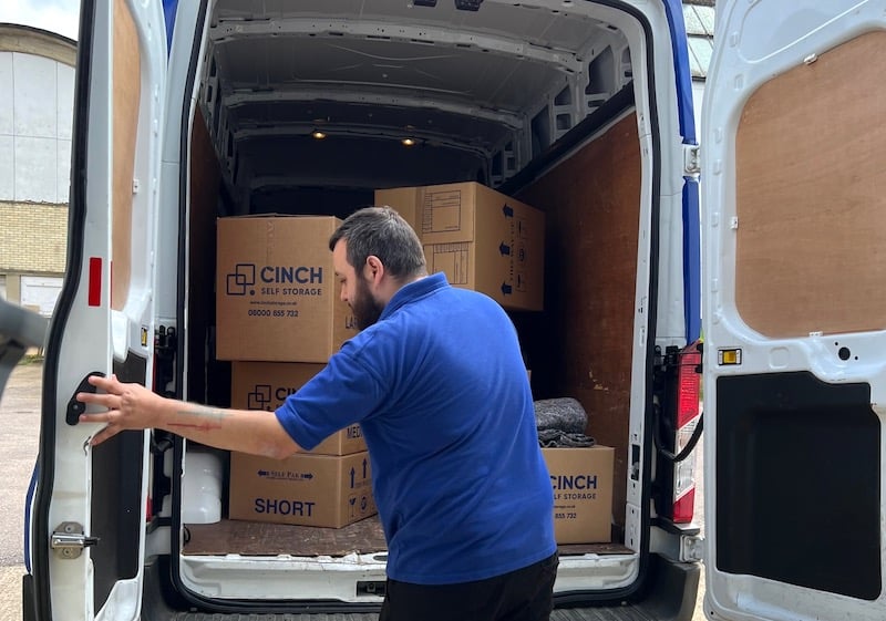 House move storage Chippenham. Image shows the open back of a van with cinch self storage cardboard boxes stacked within it and a man closing the door