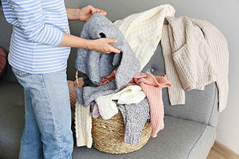Self storage Brentwood UK. Image shows a woman dressed in blue striped top and jeans taking out a jumper from a basket of winter clothes on a grey sofa