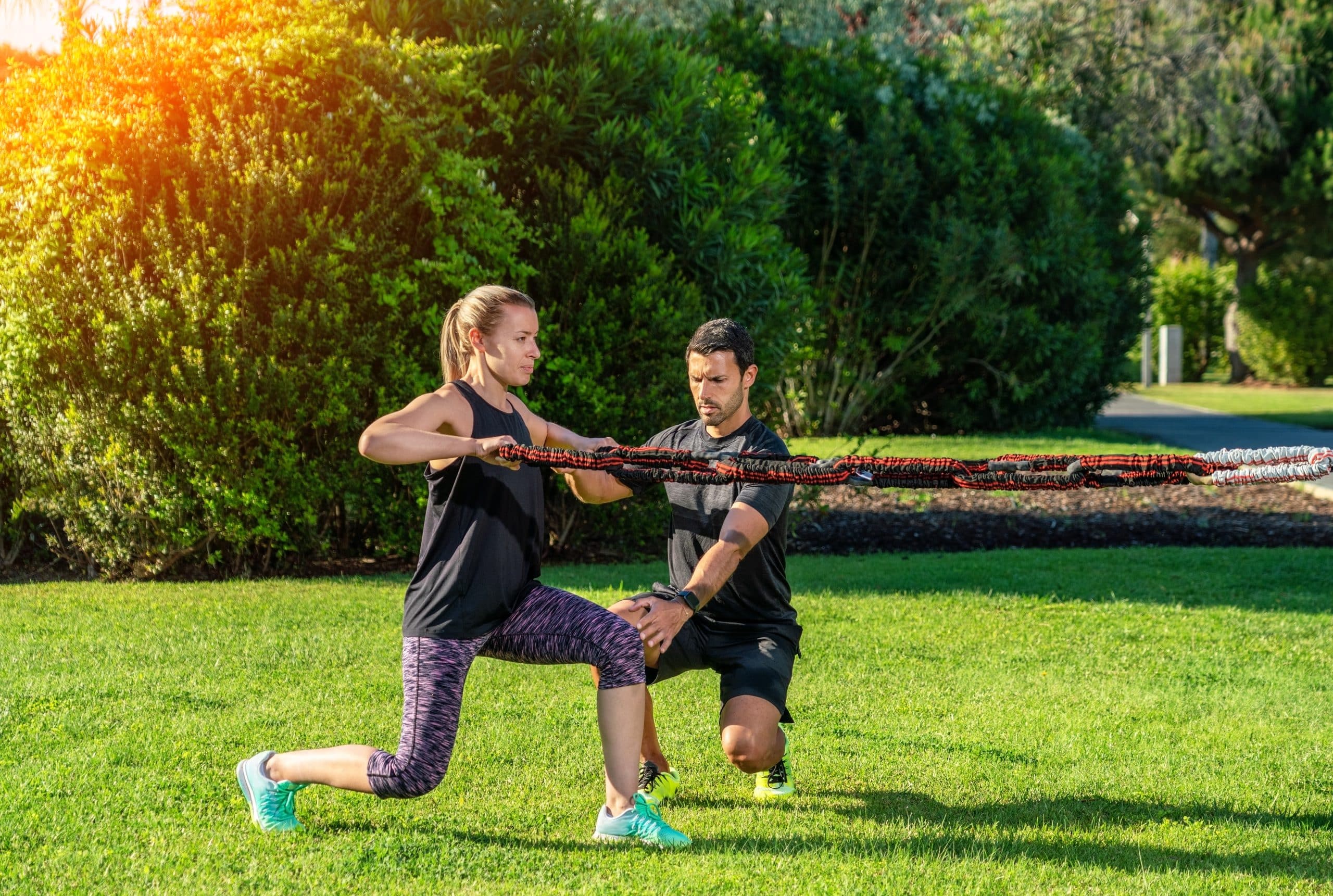 Run your own fitness business? Our rooms to rent Enfield will help. Image shows a personal trainer taking a fitness class with his female client doing lunges with ropes in a park.
