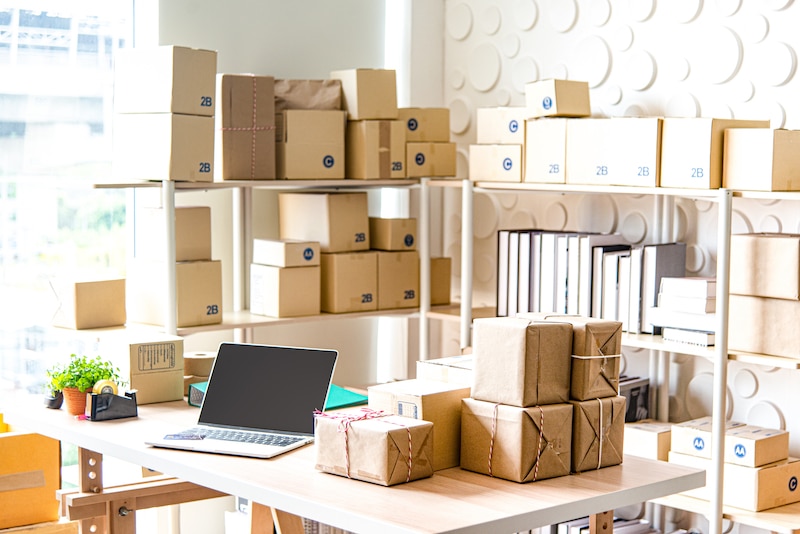 Storage Brentwood. Image shows the inside of a light and airy stockroom with brown paper parcels stacked on shelving units and a desk with an open laptop and more parcels next to it