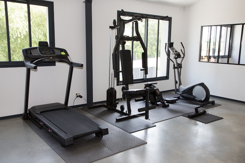 Storage units in Brentwood. Image shows a home gym set up with treadmill, weight bench and cross-trainer. With two large windows, white walls and grey flooring