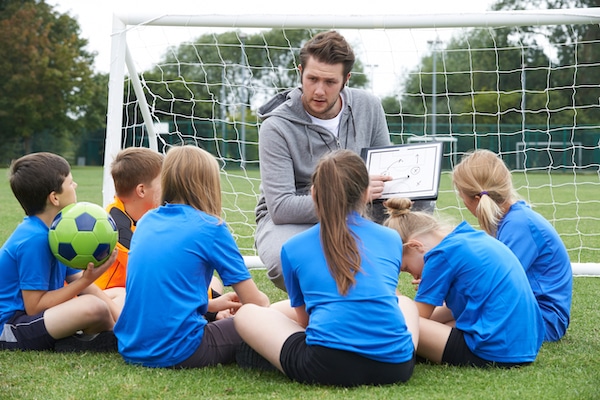 Self storage Watford. Image shows football coach kneeling down in front of goal talking to a group of kids and pointing at his drawing on a whiteboard.