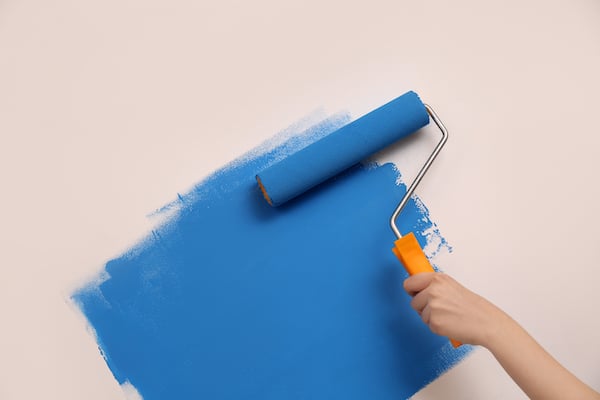 Storage unit Watford. Image shows a paint roller covered in blue paint with an orange handle, painting a wall blue. 