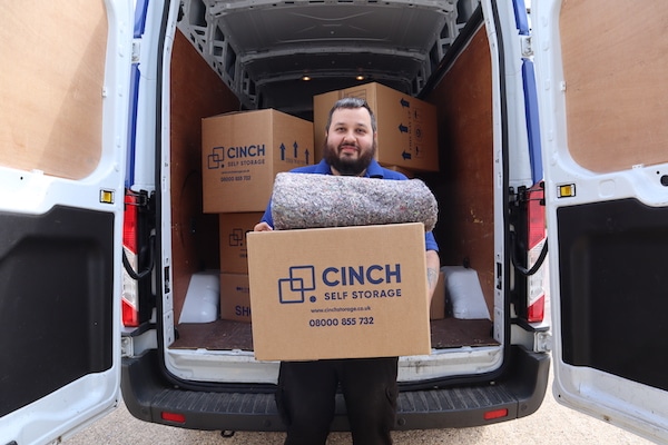 House move storage Brentwood. Image shows an open Cinch Storage Van filled with boxes with a Cinch storage employee holding a cinch cardboard box in front of the van