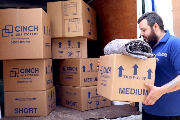 10 Tips for moving house : Your ultimate guide. Image shows a Cinch Self Storage employee holding a cardboard box filled with house move items and a dust blanket on top.