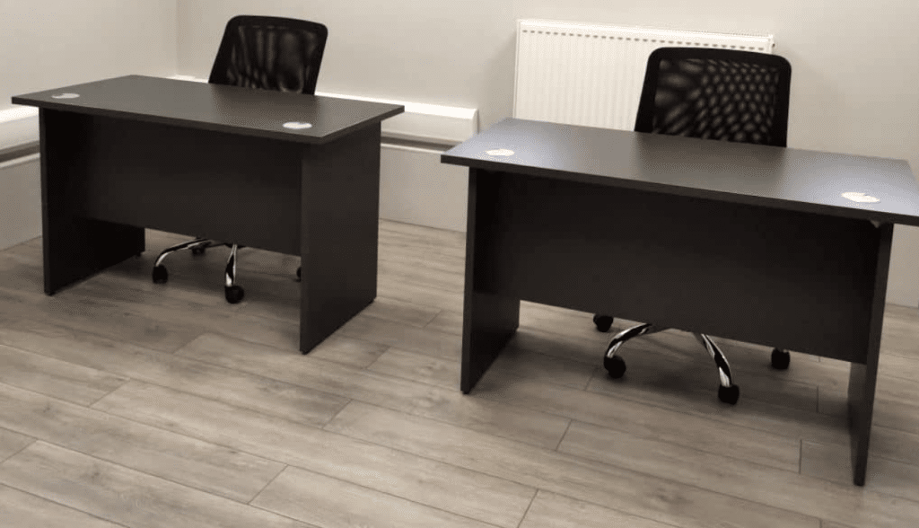 How to find the perfect office to rent in Sittingbourne. Image shows two black desks with black chairs sitting behind them. In a light grey painted office and light wood flooring.