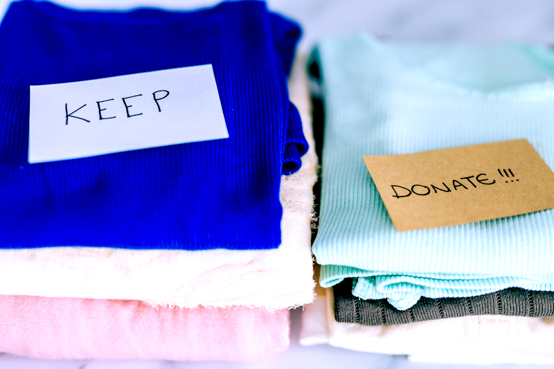 7 Life changing benefits of decluttering your space. Image shows piles of t-shirts and clothes being sorted into Keep Discard and Donate categories