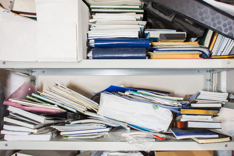 7_tips_to_declutter_your_office. Image shows a messy shelf filled with books and files. 