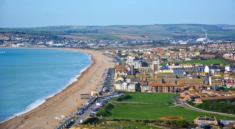 Is Seaford a nice place to live? Image shows a panoramic view of Seaford, a small coastal resort town in East Sussex, UK, from the Seaford Head, with its long beach. Seaford lies on the south coast of England, close to Seven Sisters cliffs