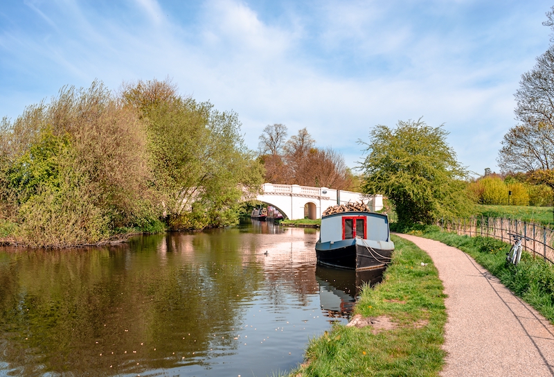 Is Watford a nice place to live? Image shows a narrow boat moored at the river Gade, Grand Union Canal. The Grove Bridge aka Grove Ornamental Bridge No 164 is in the background. Cassiobury Park, Watford, England.