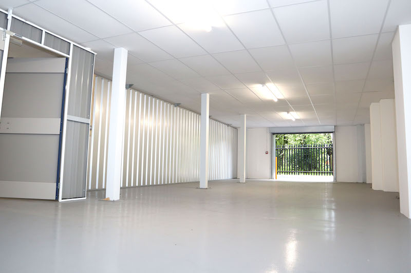 Business storage in Dunstable. Image shows an empty interior of an enterprise unit at Cinch Self Storage. With white walls, grey floor and an open roller shutter door to the outside.