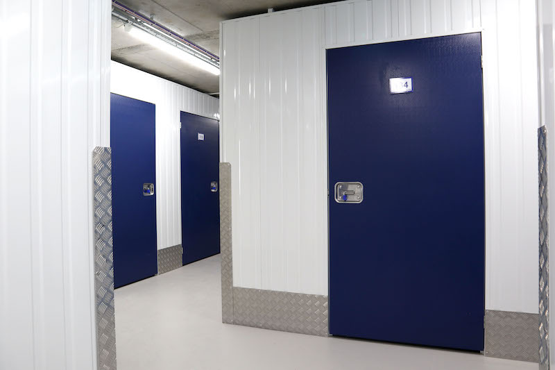 5 Reasons why you NEED self storage in Earlsfield. Image shows a corridor of a self storage facility with blue doors on the storage units and white walls.