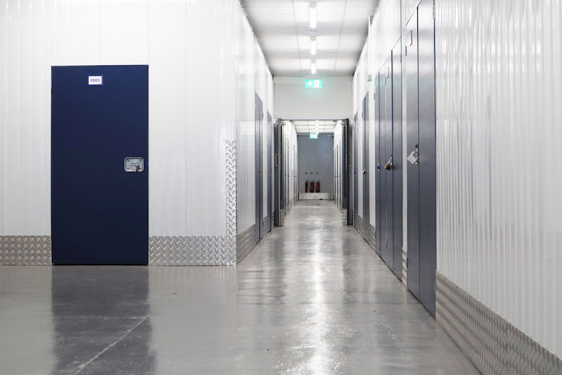 5 Tips to organise your self storage unit. Image shows a white corridor with blue doors leading to storage units.