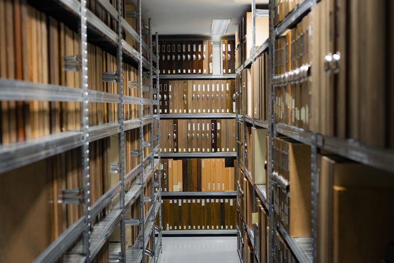 How to archive documents. Image shows a storage room with metal shelving units filled with brown archive boxes