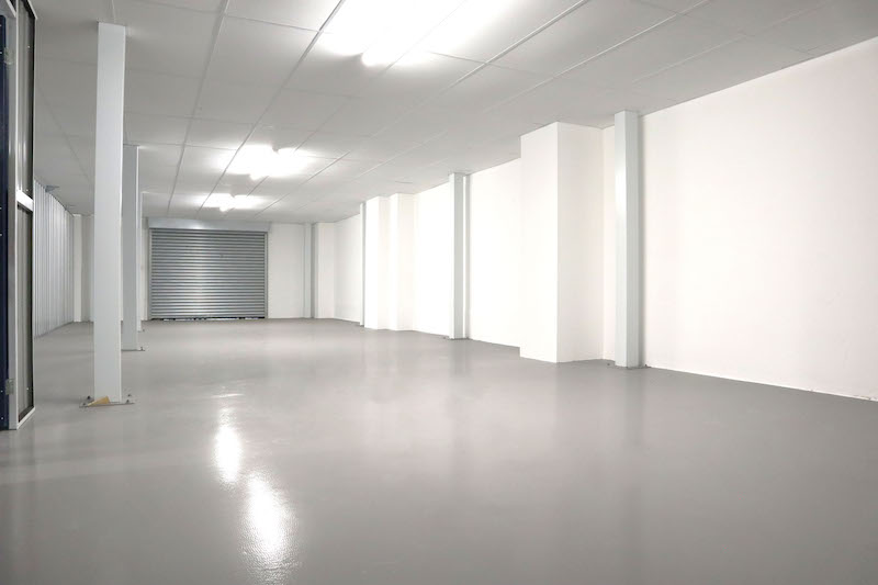 How to clean out a storage unit. Image shows lights on in an empty storage unit space with white walls and grey floor.
