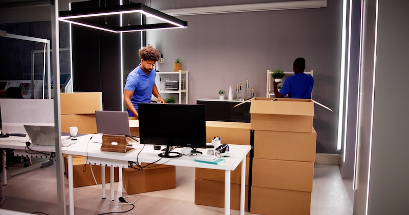 5 benefits of self storage for office moves. Image shows two men packing up a modern office with cardboard boxes