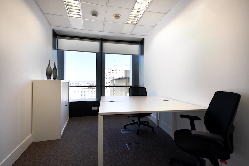 Huntingdon office space. Image shows a small office with facing office desks with black swivel chairs in an office with windows overlooking the city