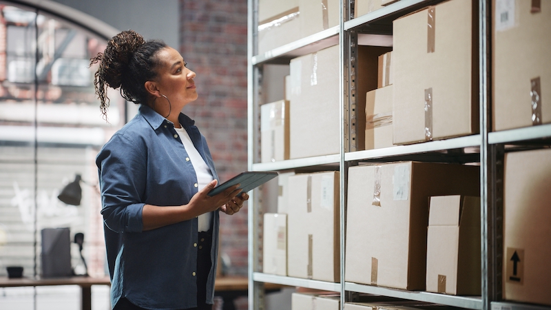 Business storage in Southend. Image shows a woman holding a tablet in front of a set of shelves filled with cardboard boxes.