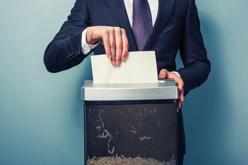 Should you shred old business documents? Image shows a businessman in a suit and tie shredding paper documents