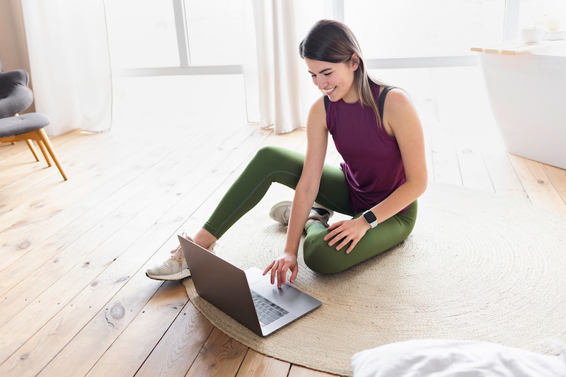 Storage Dunstable. Image shows a sporty young woman in sportswear is sitting on the floor with laptop at home.