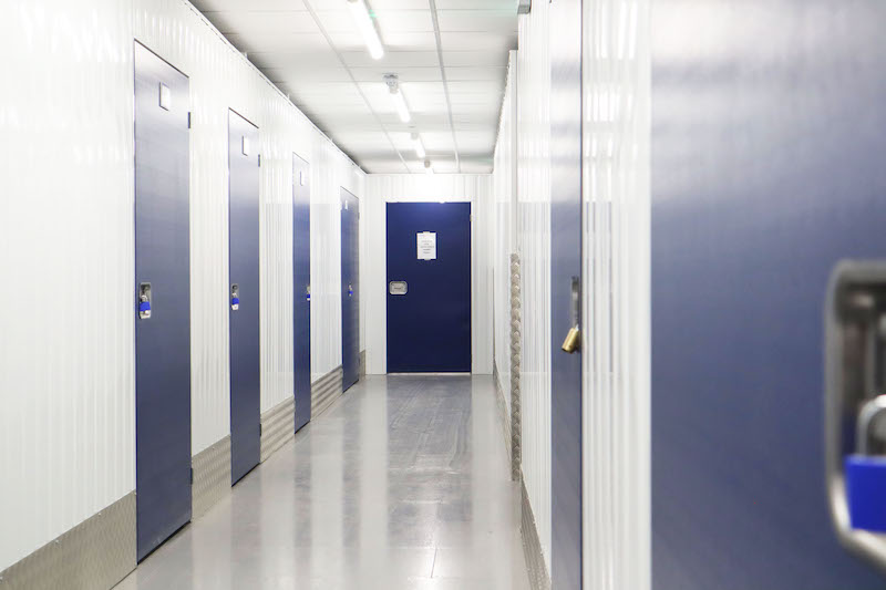 Storage unit Dunstable. Image shows a long corridor with storage units on either side with blue doors and a blue door at the end of the corridor