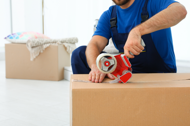 When to start packing for a house move. Image shows a man in a blue top taping up a cardboard box
