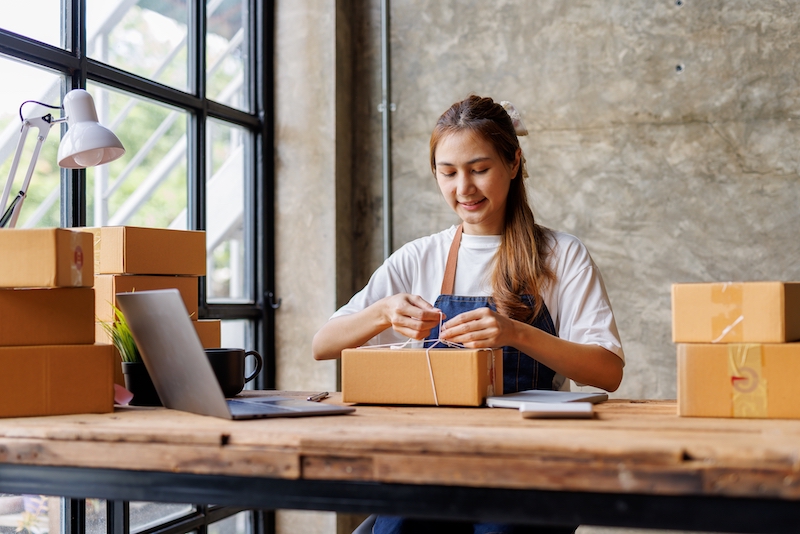 Grow your business with Self Storage. Image shows a woman at a desk, tieing up a box ready to be shipped out from her small business