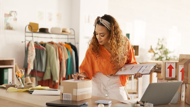 Storage space Sidcup. Image shows a woman in an orange jumper inspecting a packaged order standing with clothes on a rack behind her