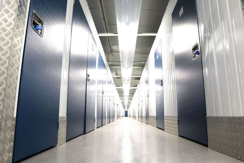 Self storage in Godmanchester. Image shows a low angle view of a corridor of storage units with blue doors.